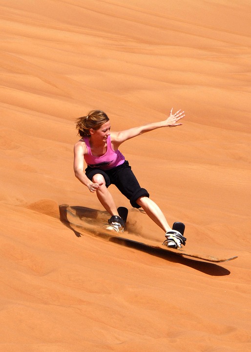 Nainen surffaa hiekalla skatelaudalla. 